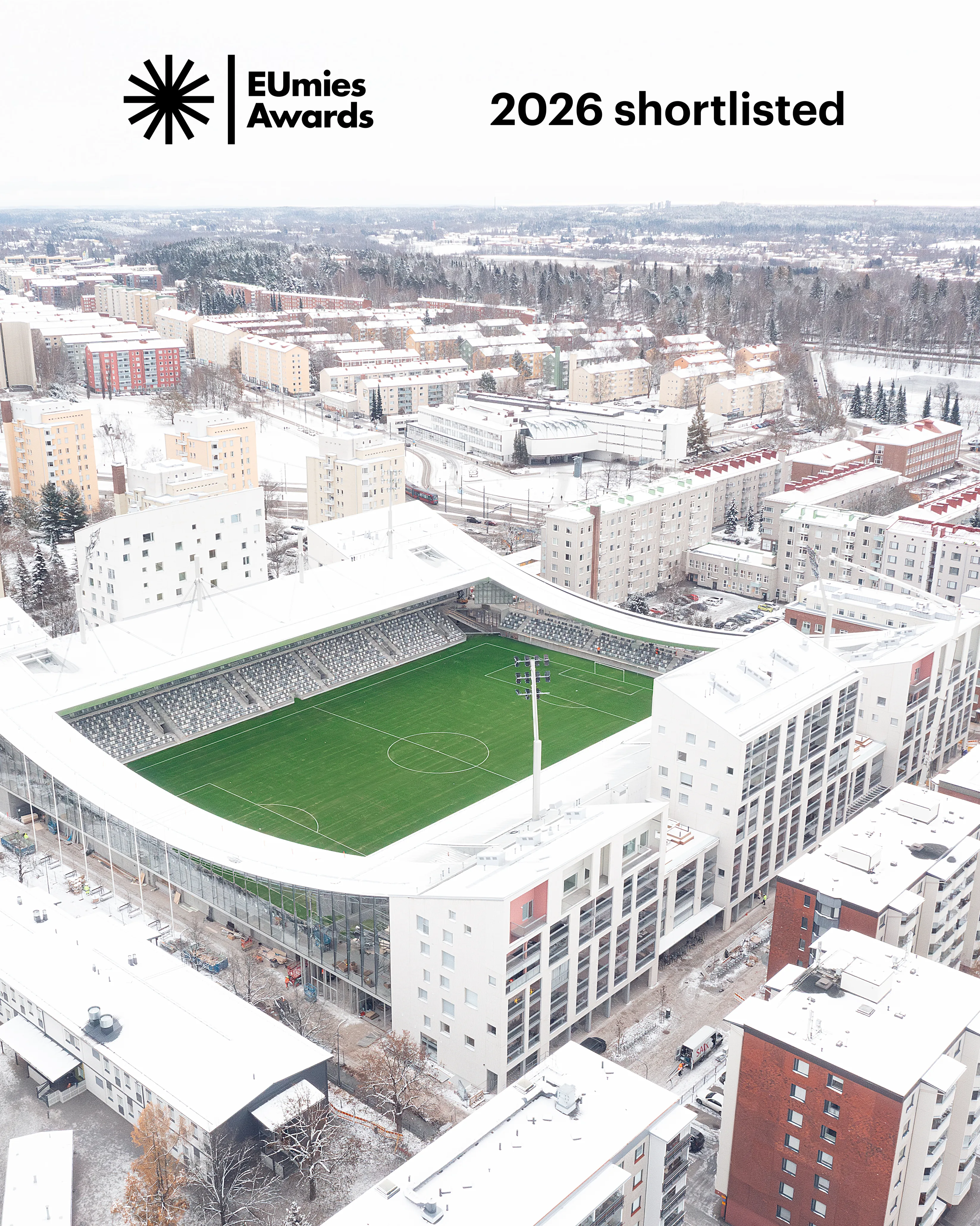 Aerial view of a modern stadium surrounded by residential buildings in a snowy landscape, showcasing the venue shortlisted for the 2026 EUmies Awards.